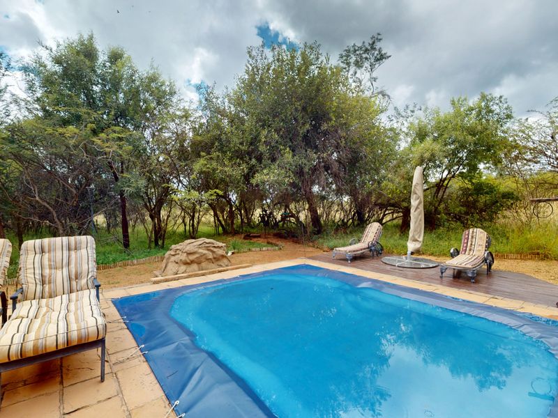 Outdoor pool area featuring a swimming pool with a cover, tiled surround, and adjacent timber decking set within a natural garden environment.