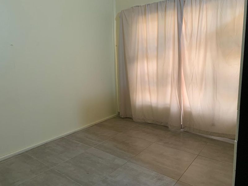 A vacant bedroom featuring neutral tiled flooring and wall-mounted curtain tracks, offering a blank canvas for personalization.