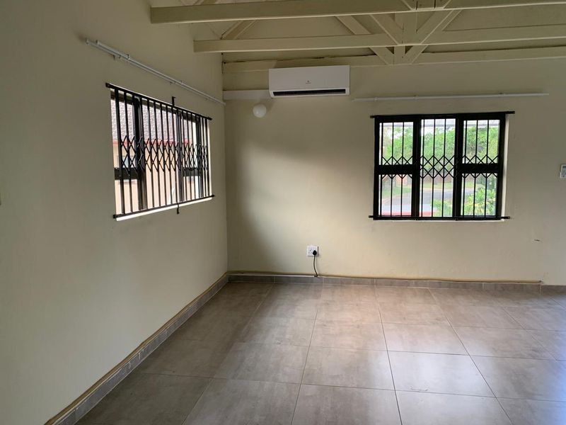 An empty living area featuring tiled floors, exposed timber ceiling beams, security bars on windows, and a wall-mounted air conditioning unit.