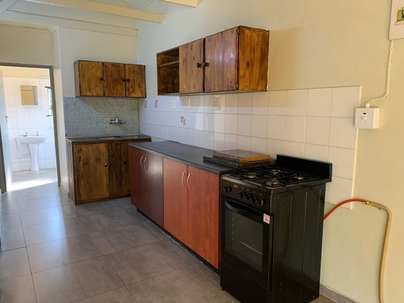 A functional kitchen featuring wooden cabinetry, a tiled backsplash, and a freestanding gas stove, with an adjacent view into a bathroom area.