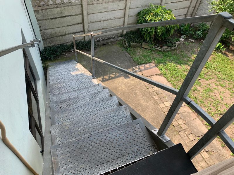 An exterior view looking down a metal staircase leading to a small rear garden area with a concrete boundary wall.
