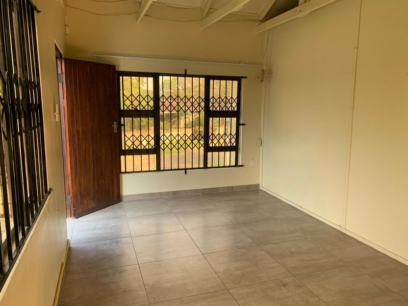 An empty living room featuring tiled flooring, exposed beam ceilings, and security gates on the windows and door.