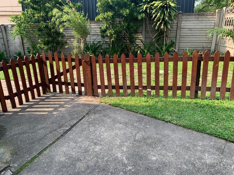 A private garden area featuring a wooden picket fence, a concrete patio, and a precast concrete boundary wall with established greenery.