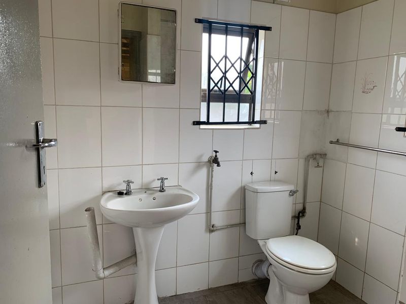 A dated bathroom featuring a pedestal basin and toilet with exposed plumbing and tiled walls, requiring renovation to modernize the space.