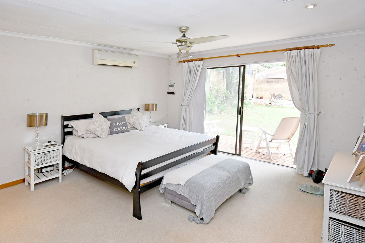 Spacious bedroom featuring a ceiling fan, wall-mounted air conditioning unit, and sliding glass doors providing direct access to the rear patio and garden.