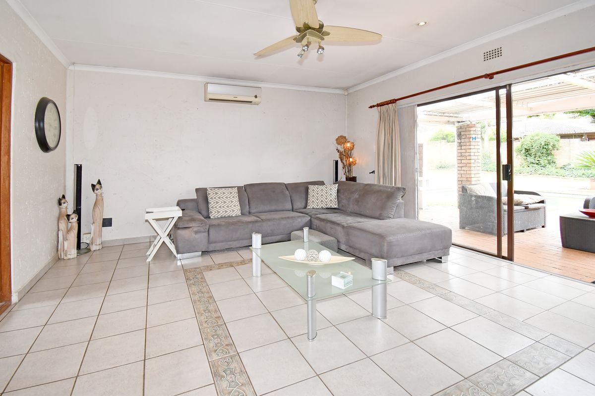 Spacious living room featuring tiled flooring, a ceiling fan, wall-mounted air conditioning unit, and large sliding glass doors leading to an outdoor patio area.