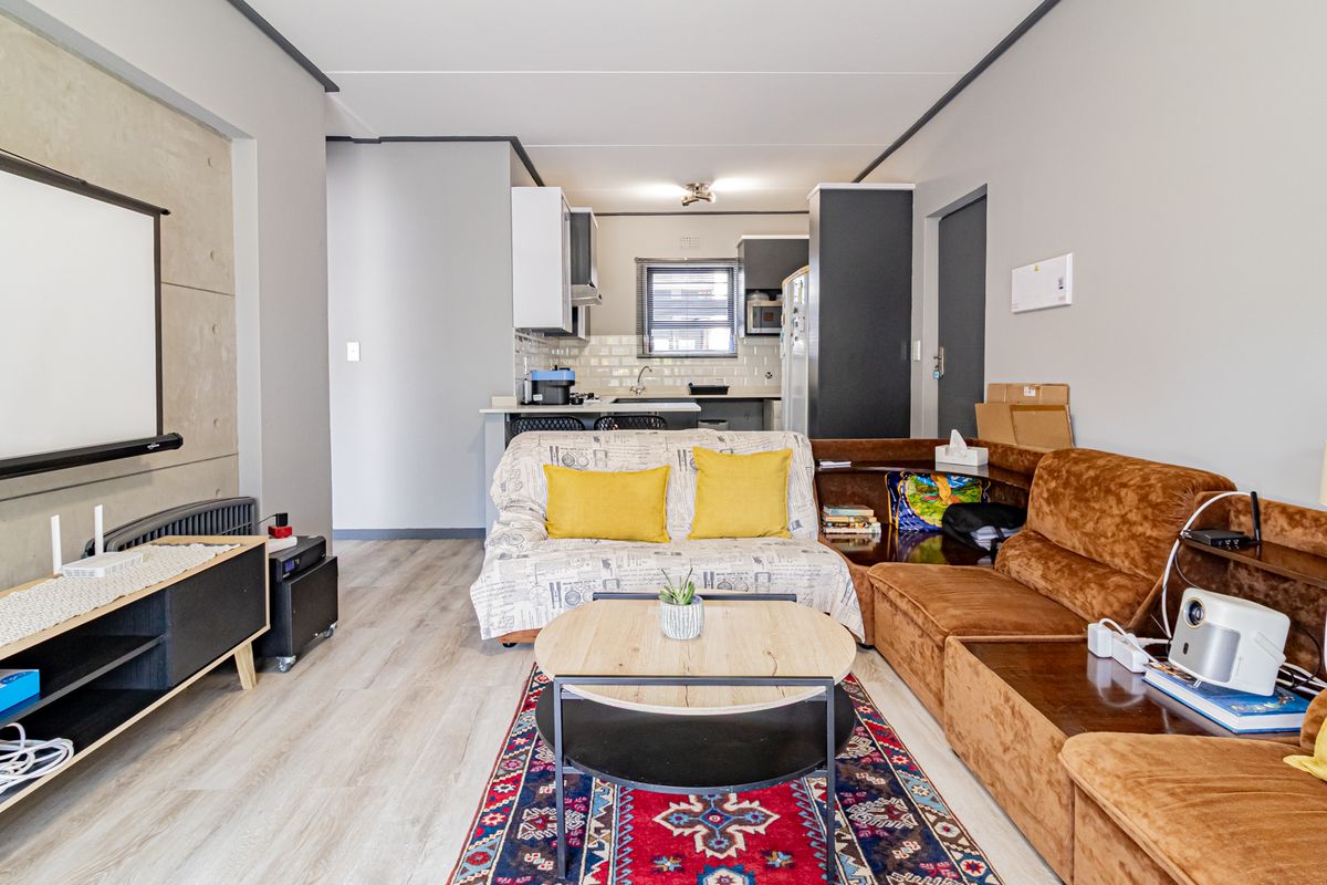 Open-plan living area featuring a modern kitchen with subway tile backsplash and a distinct concrete feature wall, seamlessly connected to the lounge space.
