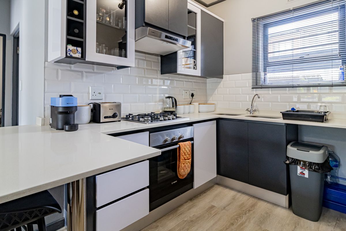 Modern kitchen featuring dark and white cabinetry, subway tile backsplash, gas hob, built-in oven, and light-toned laminate flooring.