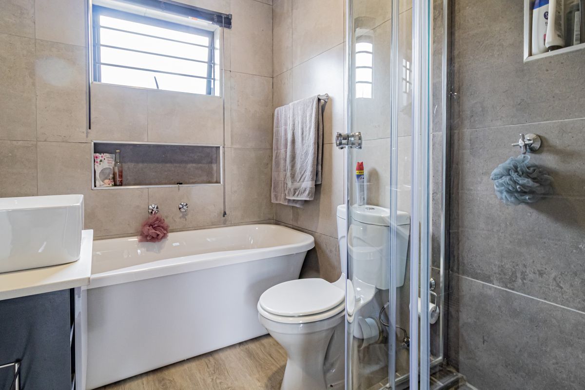 Modern bathroom featuring a freestanding bathtub, separate glass-enclosed shower, vessel sink, and neutral floor-to-ceiling tiling.