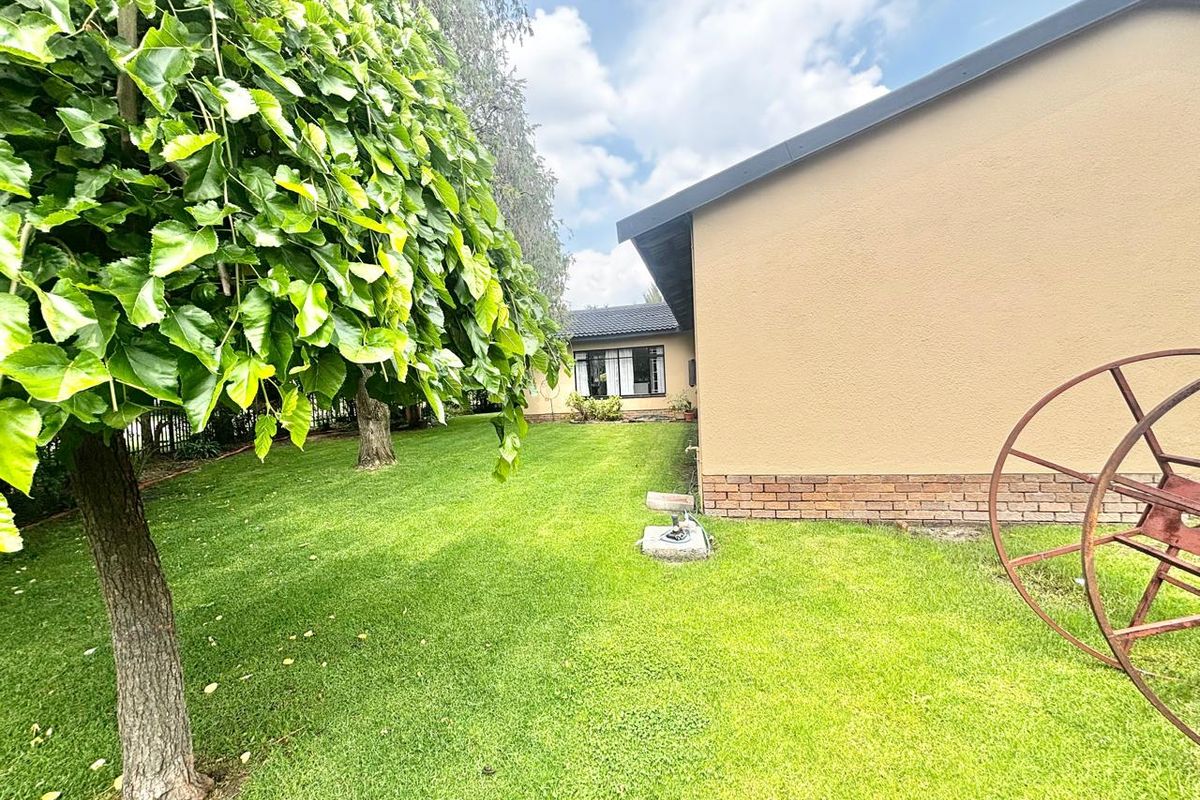 A view of the rear garden featuring a well-maintained lawn, mature tree, and the side elevation of the house with brick and plaster finishes.