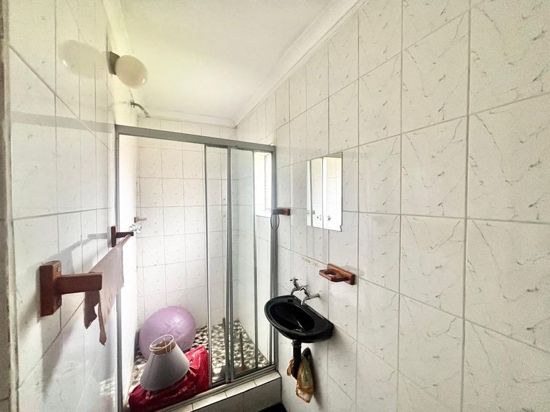 A compact bathroom featuring a shower enclosure, wall-mounted basin, and full-height wall tiling. The space would benefit from modern updates to fixtures and finishes.