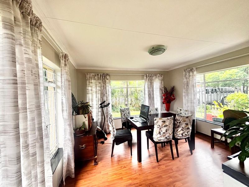 A bright dining room featuring laminate flooring and large windows that provide ample natural light and views of the garden.