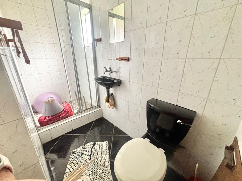 A compact bathroom featuring a shower enclosure, wall-mounted basin, and toilet with contrasting black and white tiled finishes.
