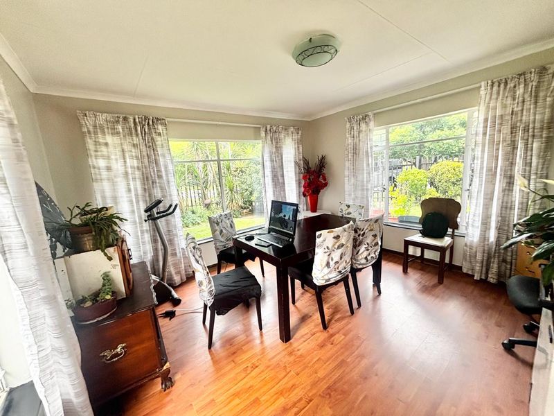A bright dining room featuring laminate flooring, large windows providing natural light, and coved cornicing, offering a functional space for family meals.