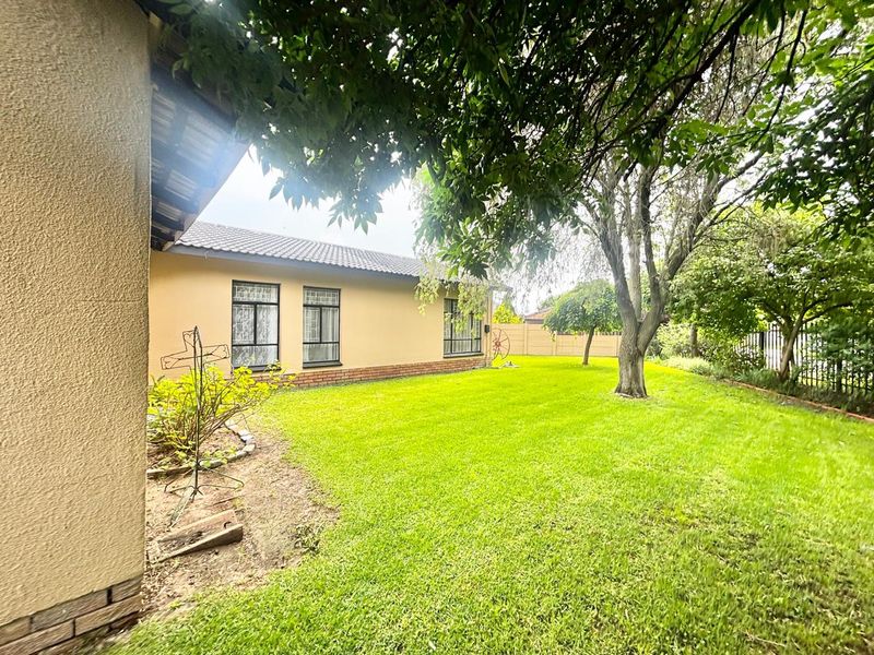 A well-maintained rear garden featuring a lush lawn, mature trees, and a clear view of the home's exterior facade with tiled roofing.