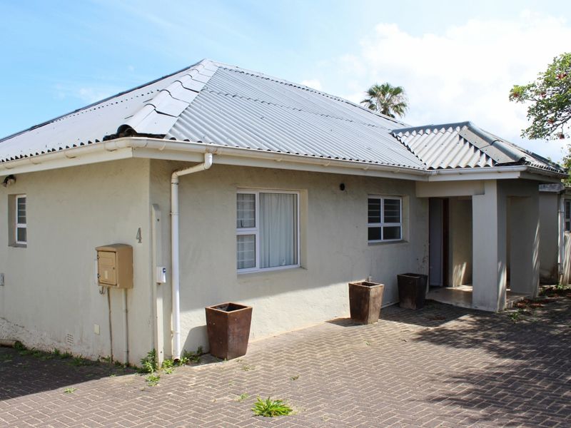 Front exterior view of a single-story house featuring a corrugated metal roof, paved driveway, and covered entrance area.