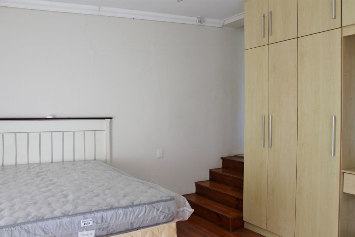 Bedroom featuring built-in light wood cupboards, timber flooring, and an internal staircase leading to an upper level.