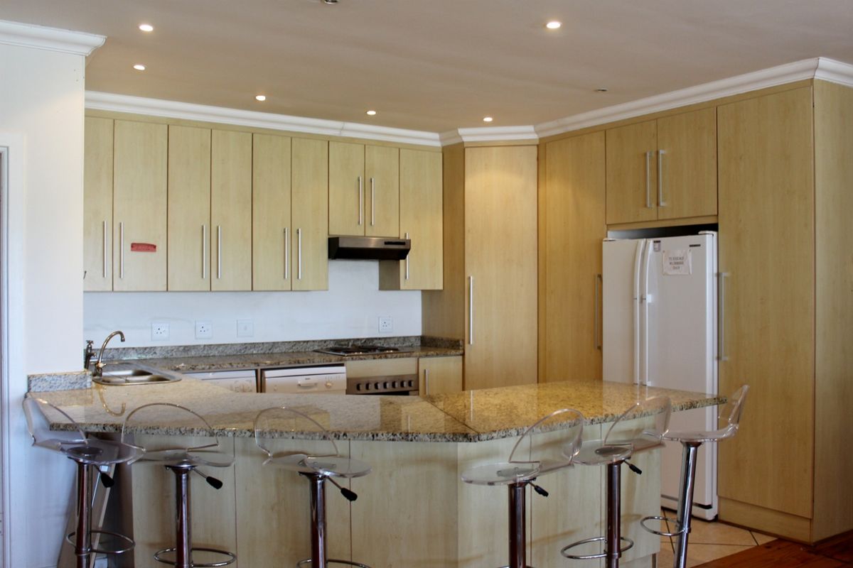 A well-maintained kitchen featuring light wood cabinetry, granite countertops, a breakfast bar, and integrated appliances with recessed ceiling lighting.