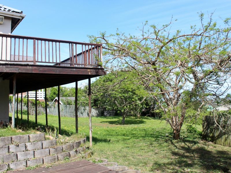 Rear view of the property featuring a raised wooden deck with balustrades, overlooking a spacious garden with mature trees and a concrete retaining wall.