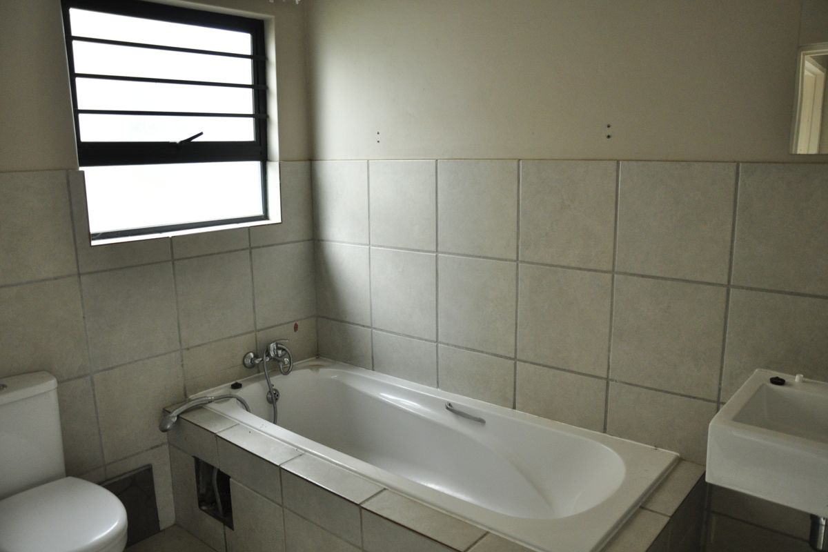 A functional bathroom featuring a built-in bathtub, wall-mounted basin, and toilet with neutral wall tiling and a horizontal window.