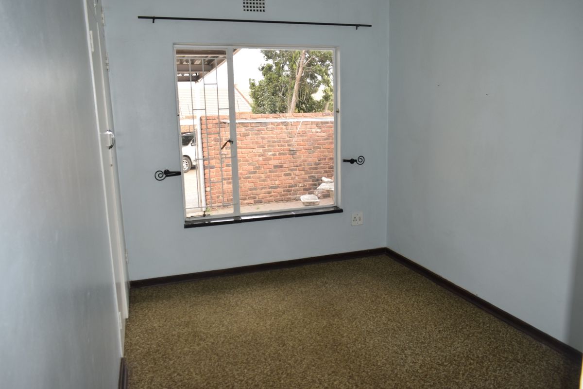 An empty bedroom featuring carpet flooring, a built-in cupboard, and a window with security bars overlooking the rear exterior area.