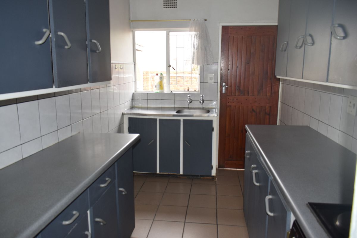A functional kitchen featuring dark blue cabinetry, laminate countertops, tiled splashbacks, and direct access to an exterior door.