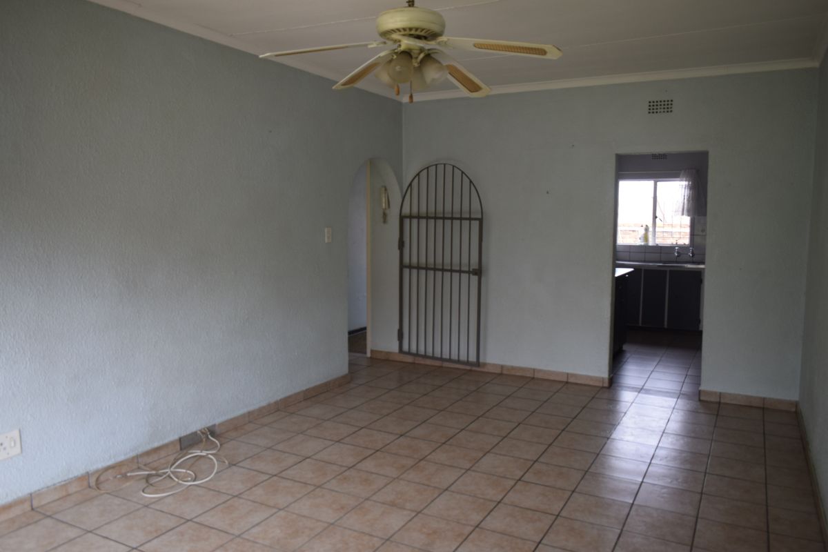 An empty living room featuring tiled flooring, a ceiling fan, and an arched doorway leading to the kitchen area.
