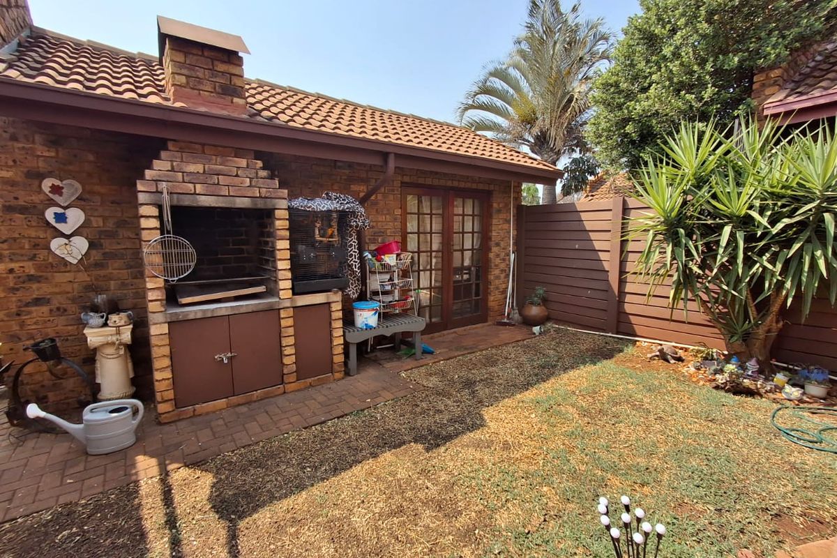 Rear garden area featuring a built-in brick braai, paved patio space, and direct access to the home through timber-framed glass doors.
