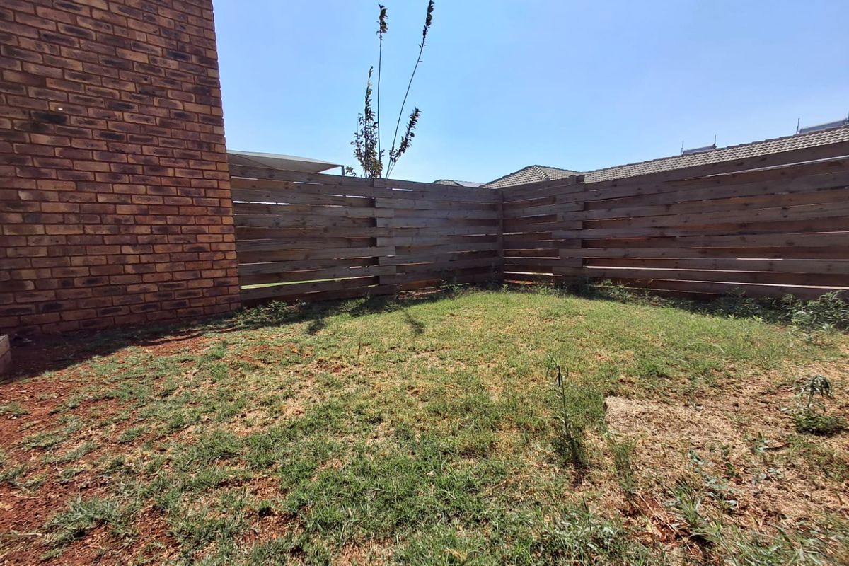 A private rear garden area featuring a brick wall and timber slat fencing, currently requiring landscaping and lawn maintenance.