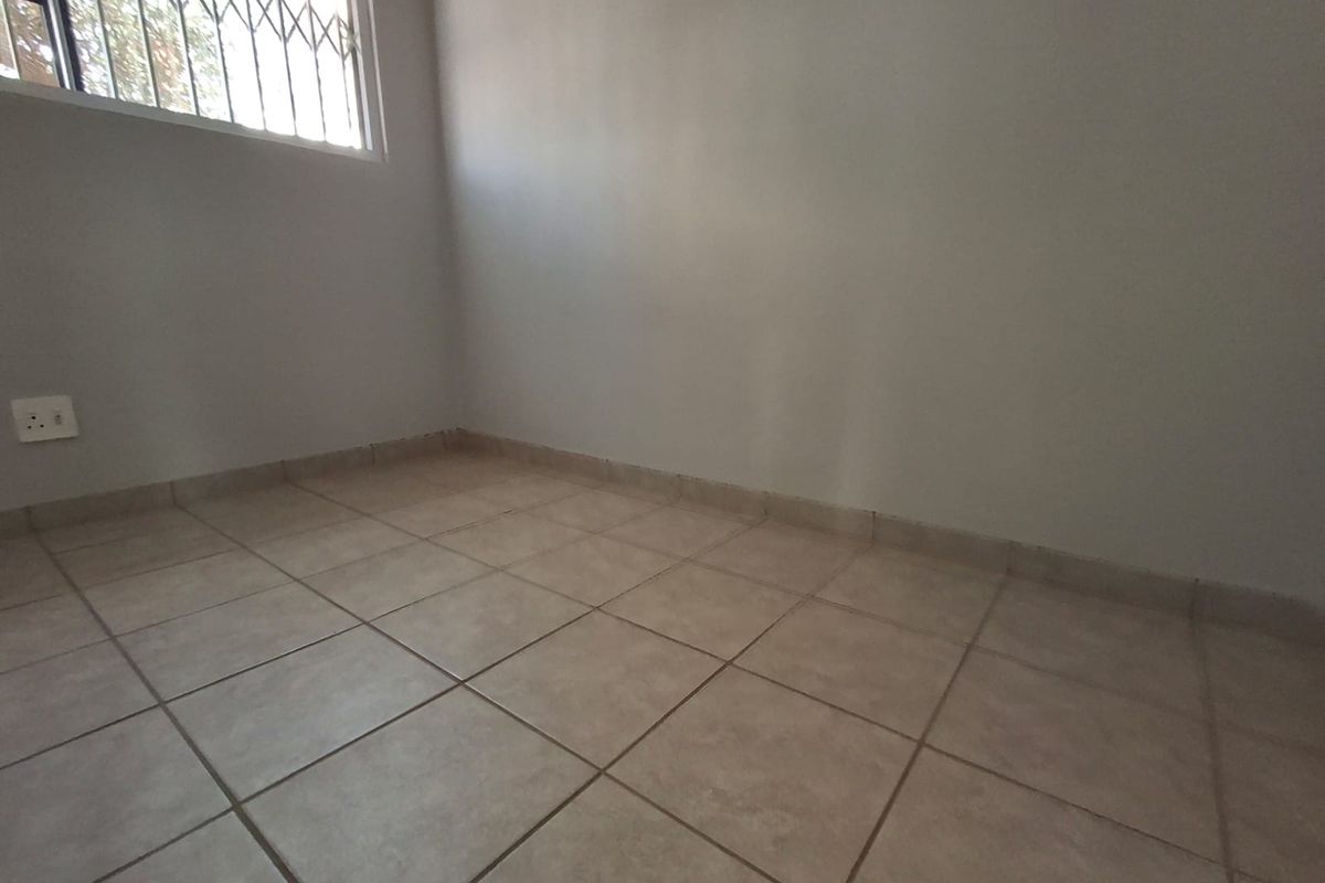 A vacant bedroom featuring neutral ceramic floor tiles, a security gate on the window, and a clean, minimalist aesthetic ready for personalization.
