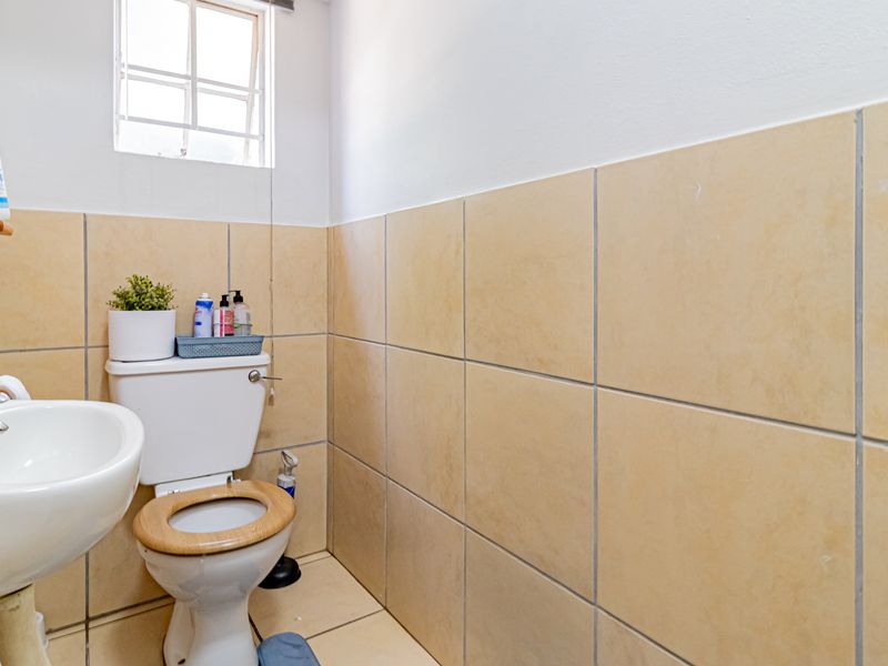 A functional guest bathroom featuring neutral ceramic wall and floor tiling, a pedestal basin, and a standard close-coupled toilet.