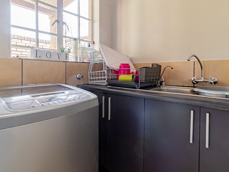 A functional laundry area featuring built-in dark cabinetry, a stainless steel sink, and a tiled splashback with natural light from the window.