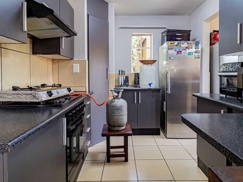 A functional kitchen featuring dark cabinetry, laminate countertops, a gas hob with extractor fan, and tiled flooring with a neutral backsplash.