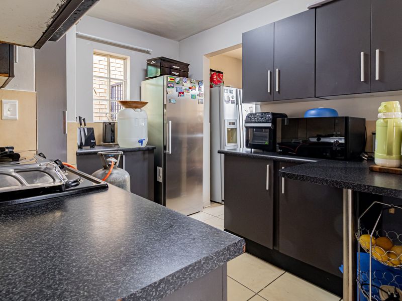 A functional kitchen featuring dark cabinetry, laminate countertops, a gas hob with extractor fan, and tiled flooring, with an adjacent scullery area.