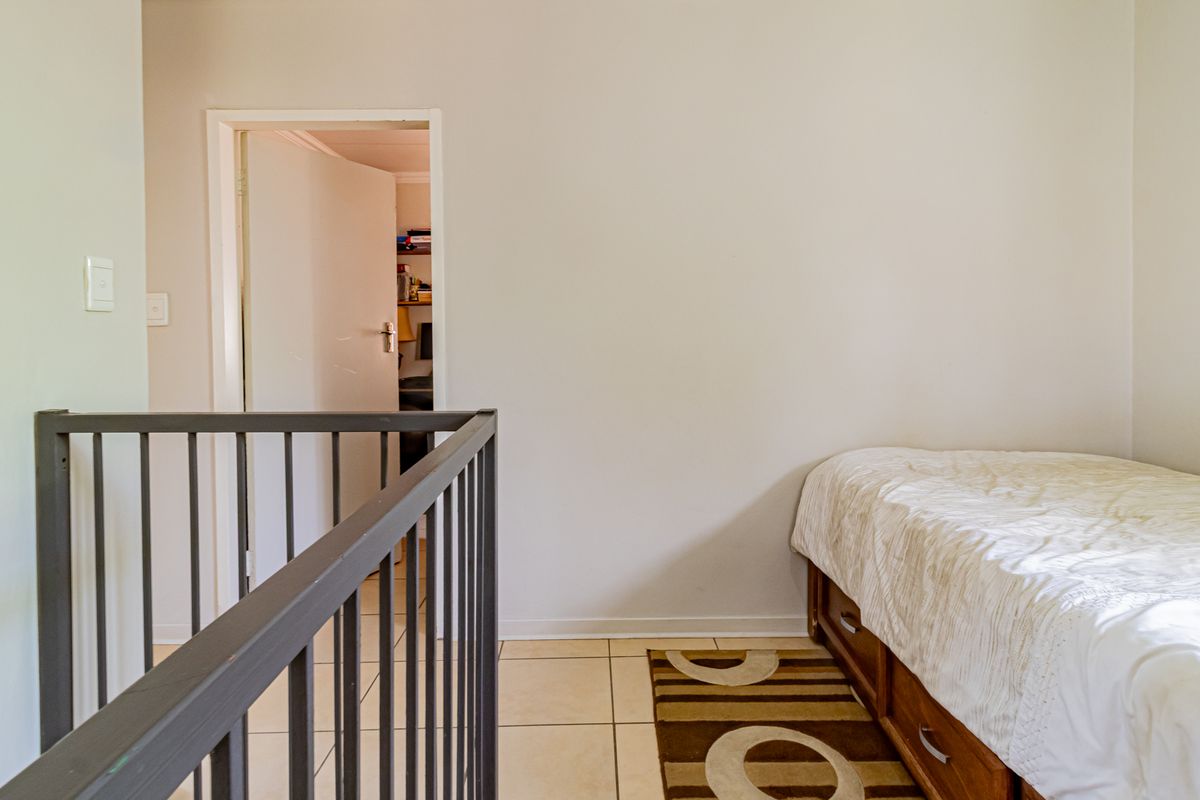 A bedroom featuring tiled flooring and a metal balustrade overlooking the lower level, with a doorway leading to an adjacent room.