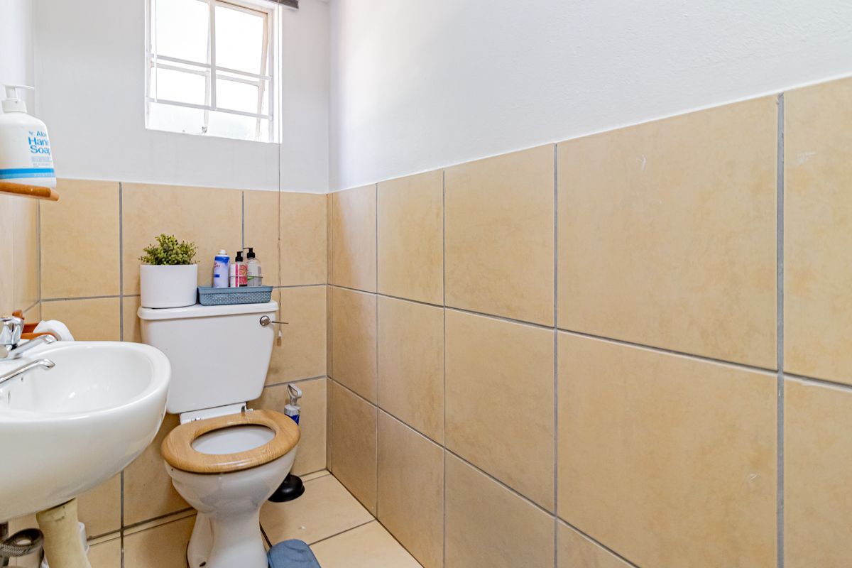 A functional guest bathroom featuring neutral ceramic wall and floor tiling, a pedestal basin, and a standard close-coupled toilet.