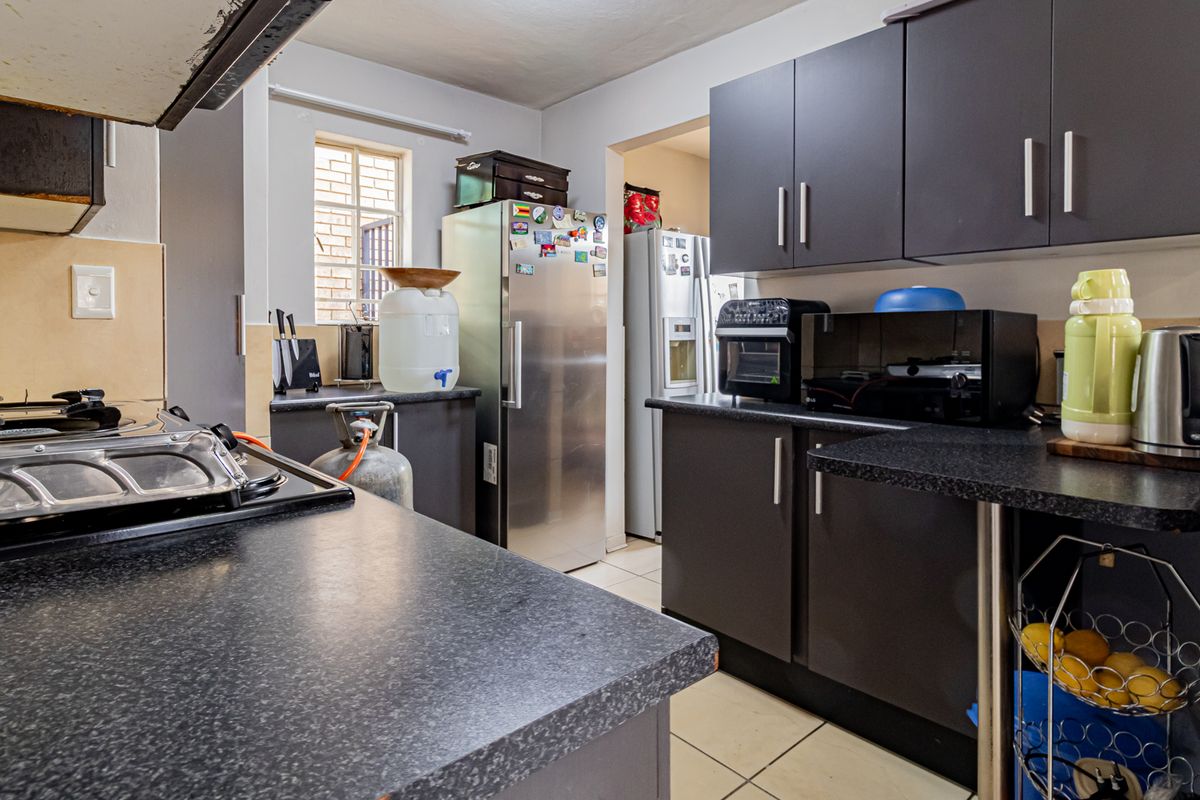 A functional kitchen featuring dark cabinetry, laminate countertops, a gas hob with extractor fan, and tiled flooring, with an adjacent scullery area.
