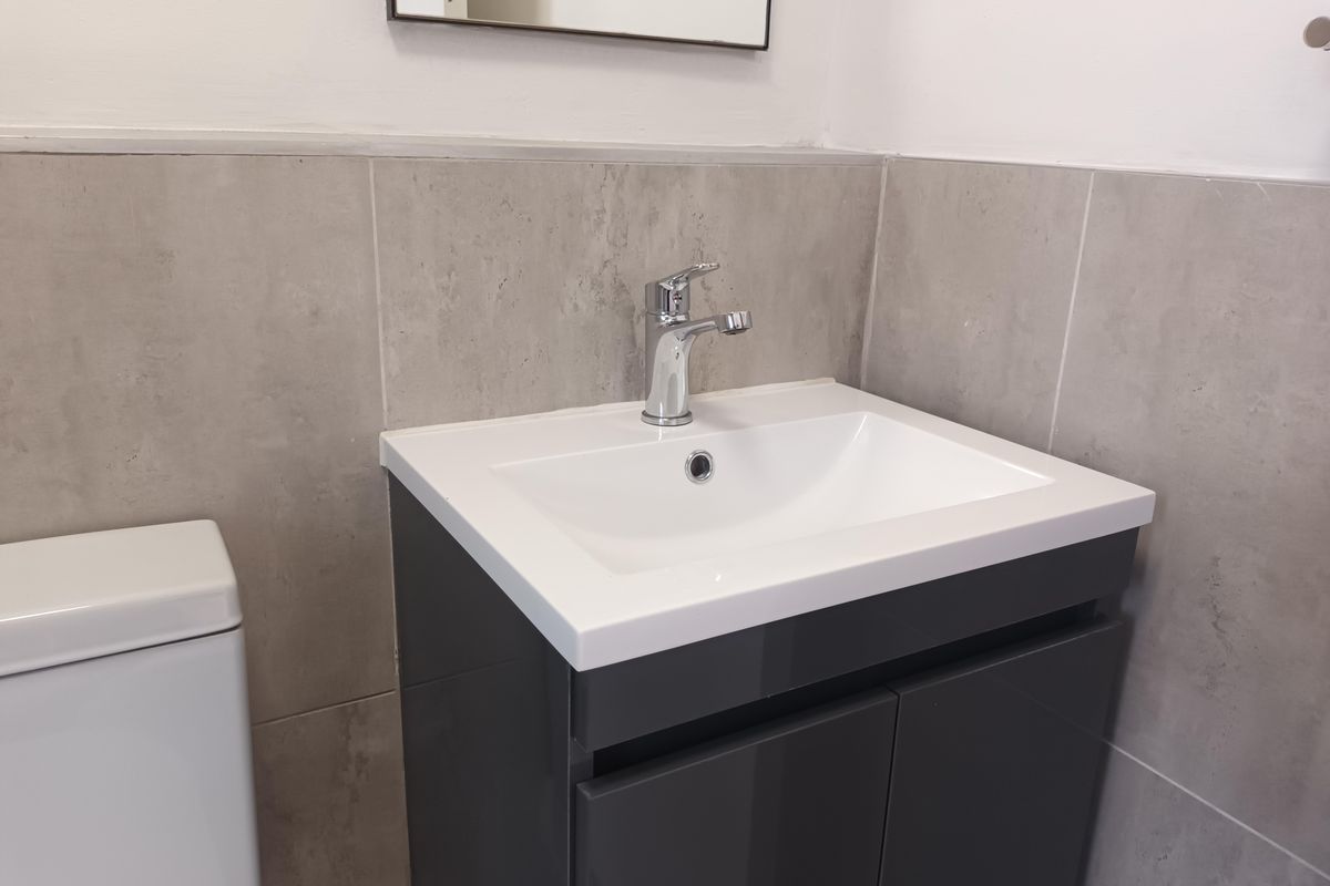 Modern bathroom featuring a sleek vanity cabinet with a white basin, chrome faucet, and contemporary grey wall tiling.
