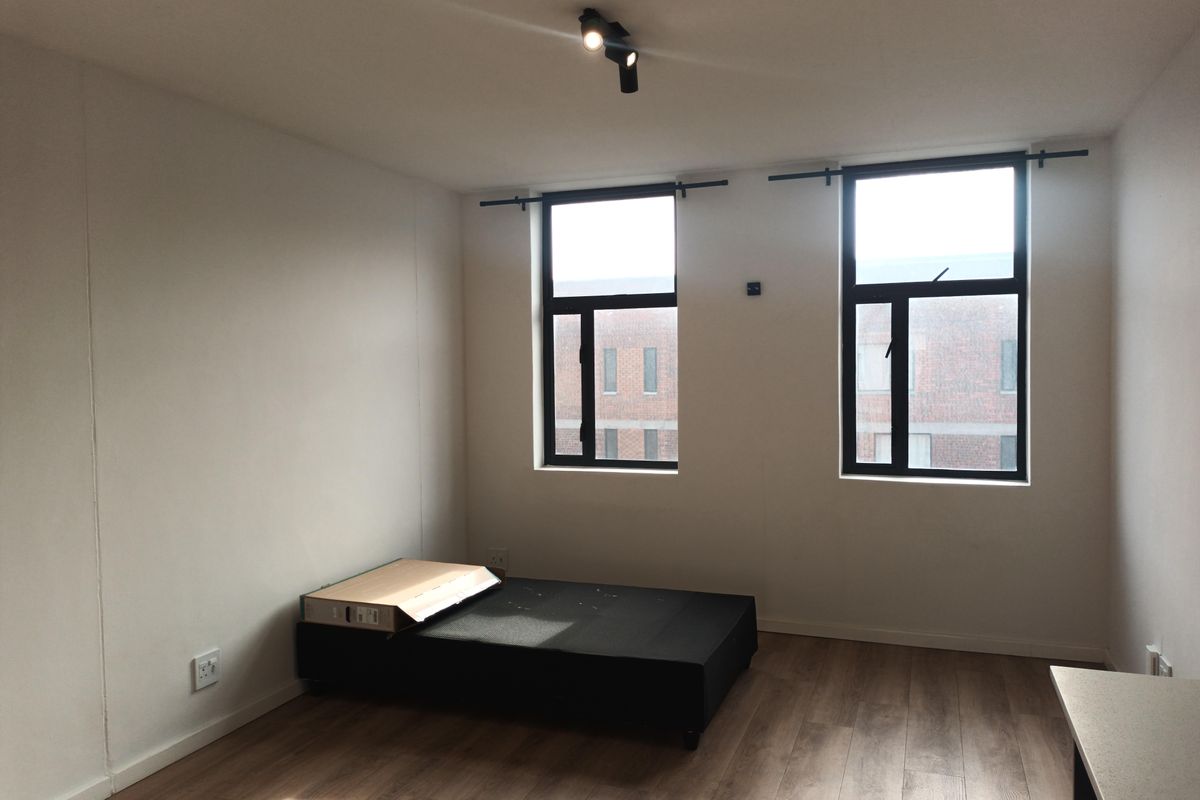 A bright, modern bedroom featuring wood-look flooring, dual windows with black frames, and contemporary track lighting.