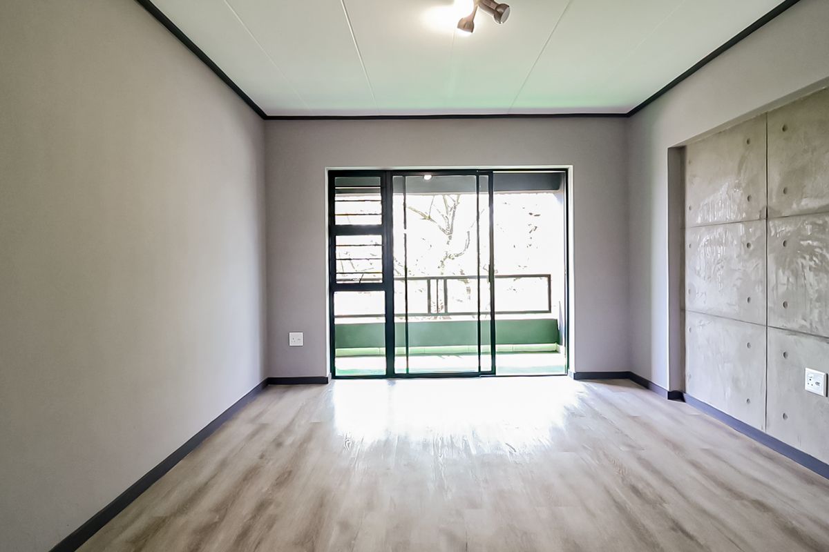 Bright and spacious living area featuring modern laminate flooring, a contemporary concrete feature wall, and direct access to an outdoor balcony through sliding doors.