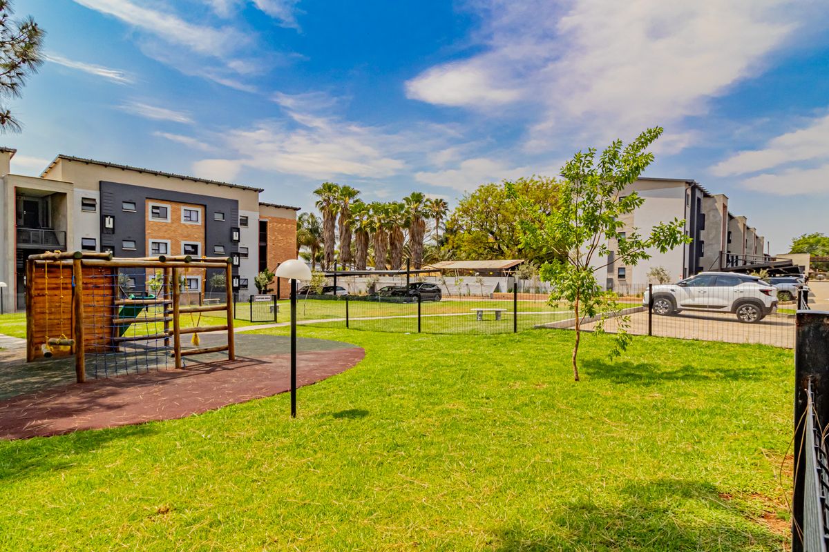 Communal outdoor area featuring a playground, landscaped garden, and paved parking access within a modern townhouse complex.