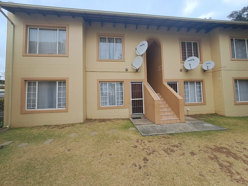Exterior view of a two-story apartment block featuring a tiled staircase, security gate, and multiple satellite dishes mounted on the facade.