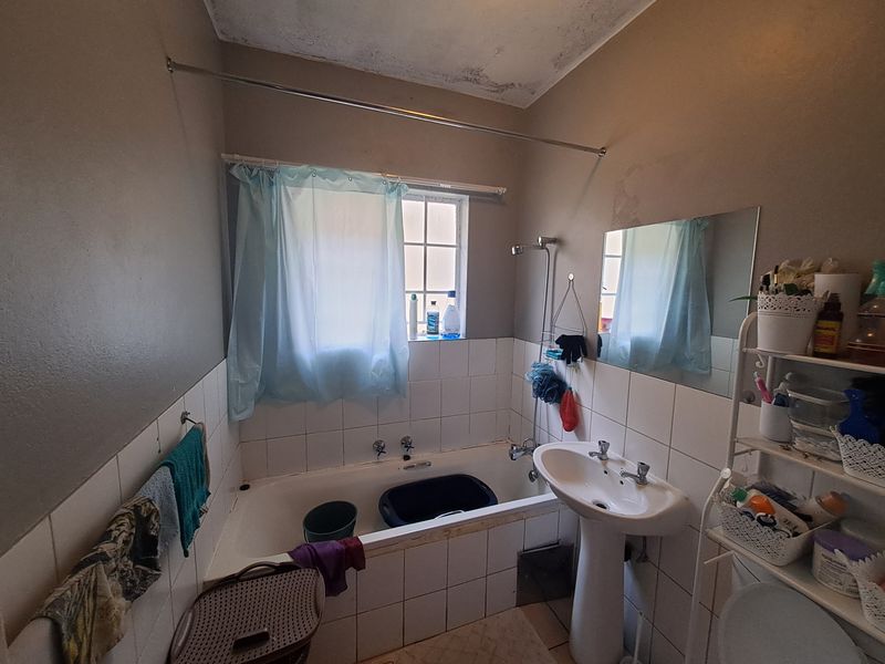 A dated bathroom featuring a pedestal basin and bathtub with tiled splashbacks, showing signs of ceiling water damage and general wear.