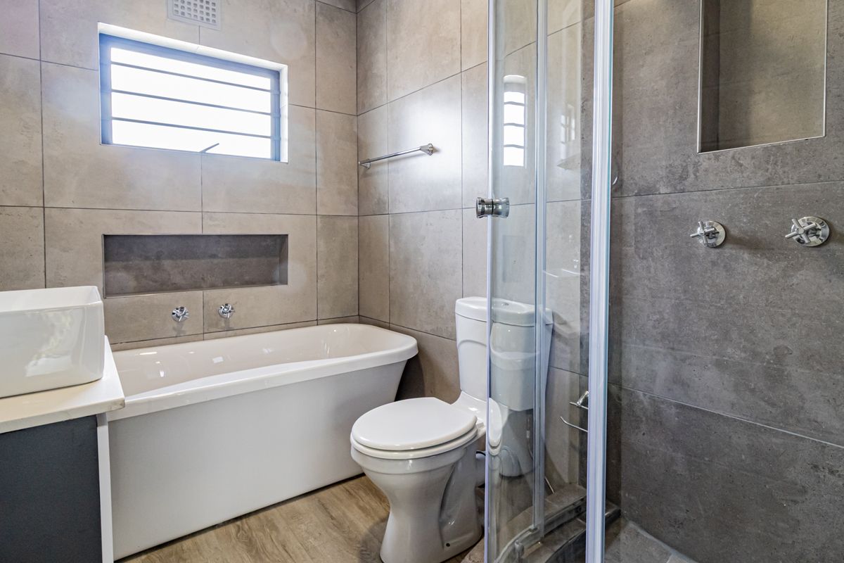 Modern bathroom featuring a freestanding bathtub, glass-enclosed shower, vessel sink vanity, and neutral floor-to-ceiling tiling with a convenient recessed wall niche.