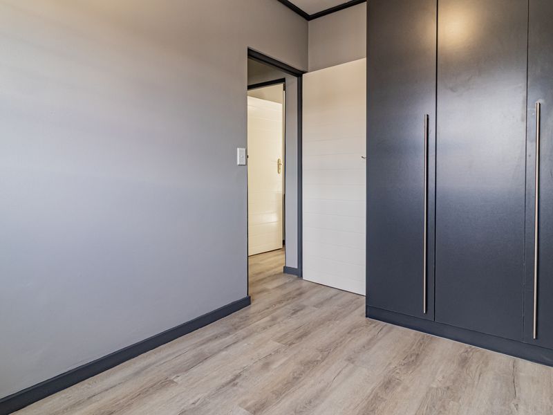 A clean, empty bedroom featuring modern dark built-in cupboards, light laminate flooring, and neutral grey walls.