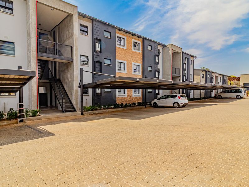 Modern townhouse complex exterior featuring paved parking area, covered carports, and multi-level residential units with external staircases and balconies.