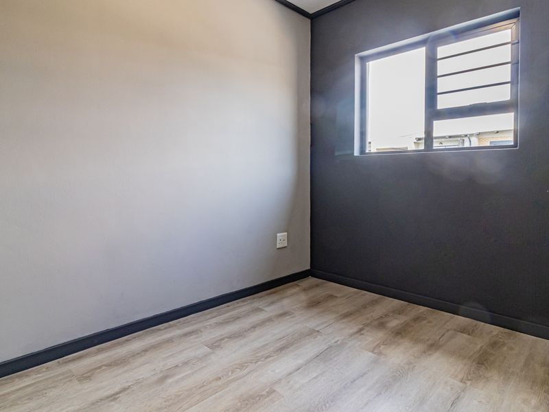 An empty bedroom featuring modern laminate flooring, contrasting grey and dark feature walls, and a window fitted with security bars.