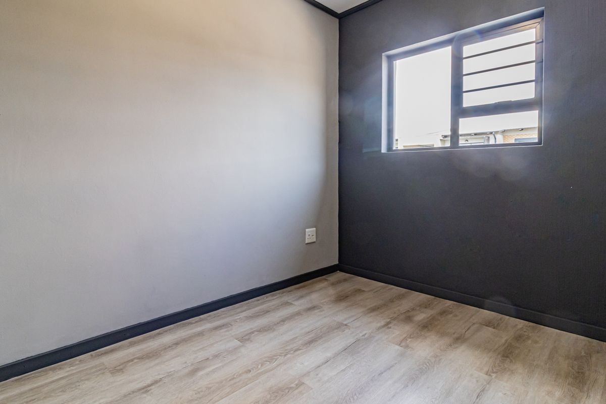 An empty bedroom featuring modern laminate flooring, contrasting grey and dark feature walls, and a window fitted with security bars.