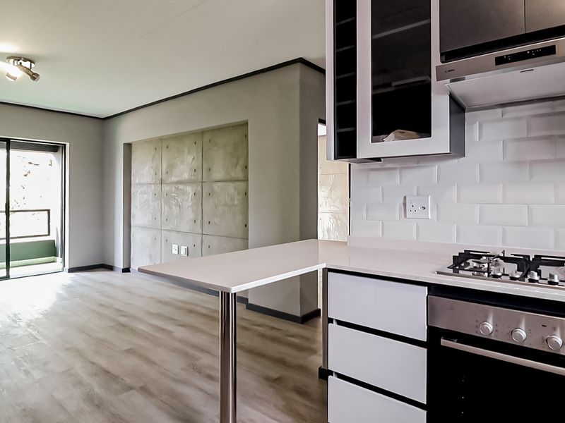 Modern open-plan kitchen and living area featuring a gas hob, subway tile backsplash, concrete feature wall, and sliding doors leading to a balcony.