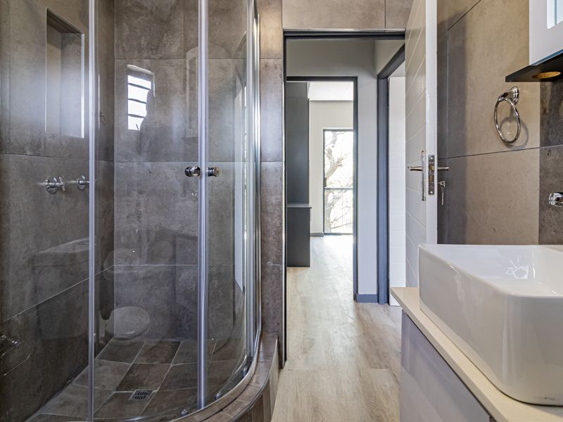 Modern bathroom featuring a curved glass shower enclosure, contemporary vessel sink with chrome fixtures, and neutral large-format wall tiles.